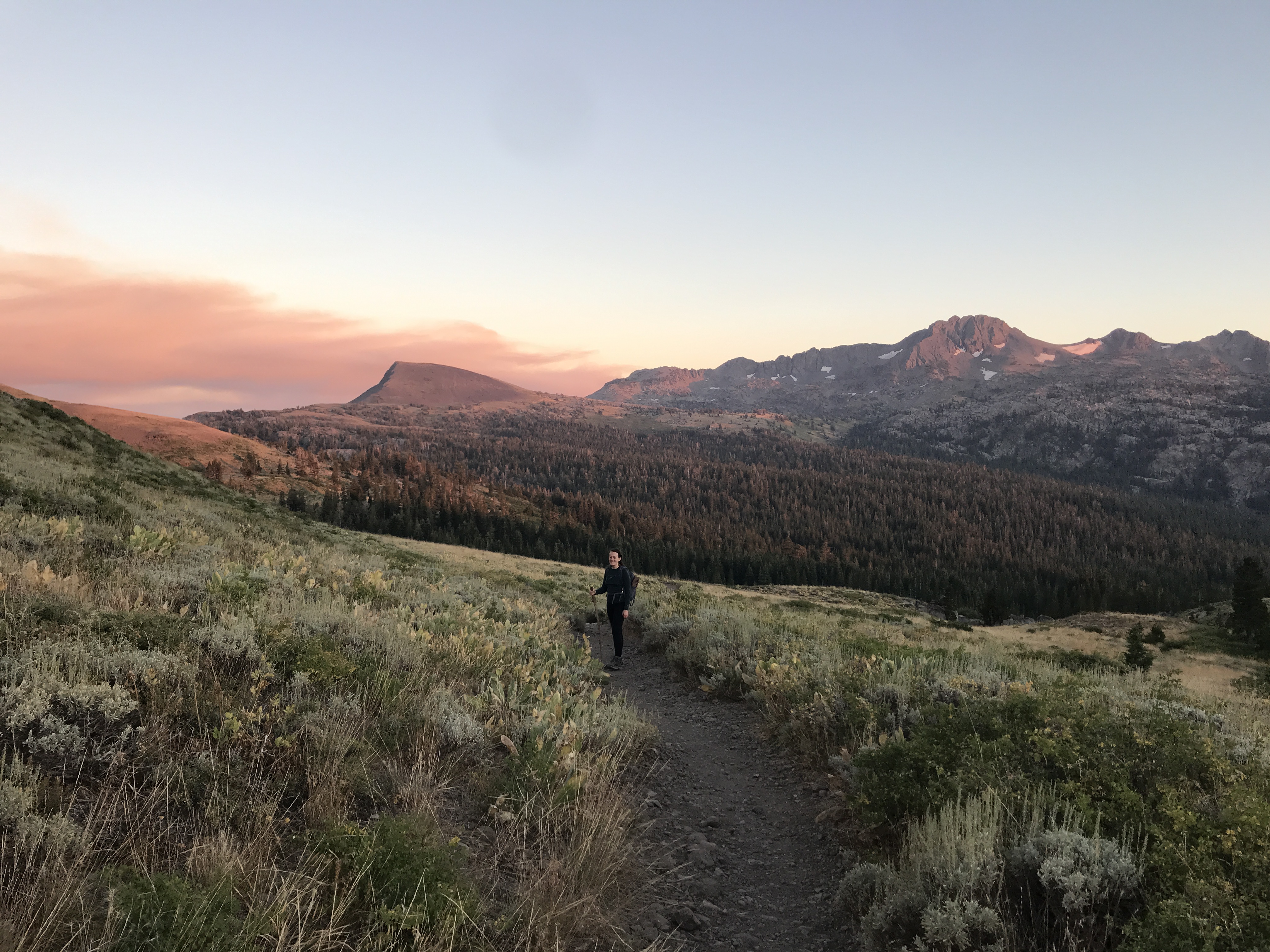 Carla on an alpine trail at sunset with mountains in the distance